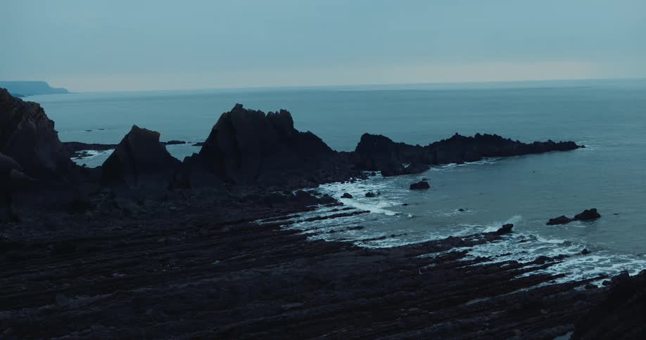 Waves roll in alongside a rocky promontory over a rocky coastline