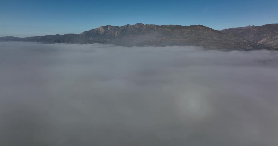 A mountain ridge stands tall among thick fog under a blue sky