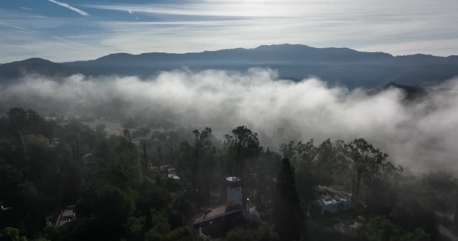 Fog covers a forested neighborhood with mountains on the horizon