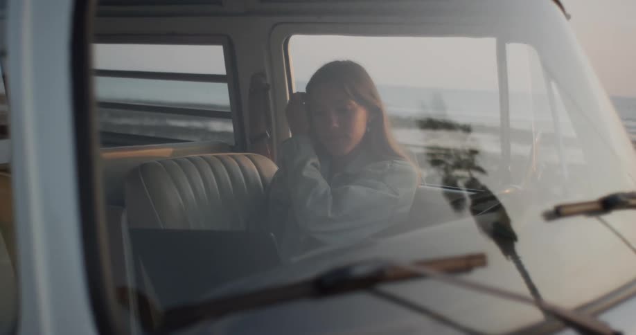 Woman sits in vehicle parked near beach and types on a laptop