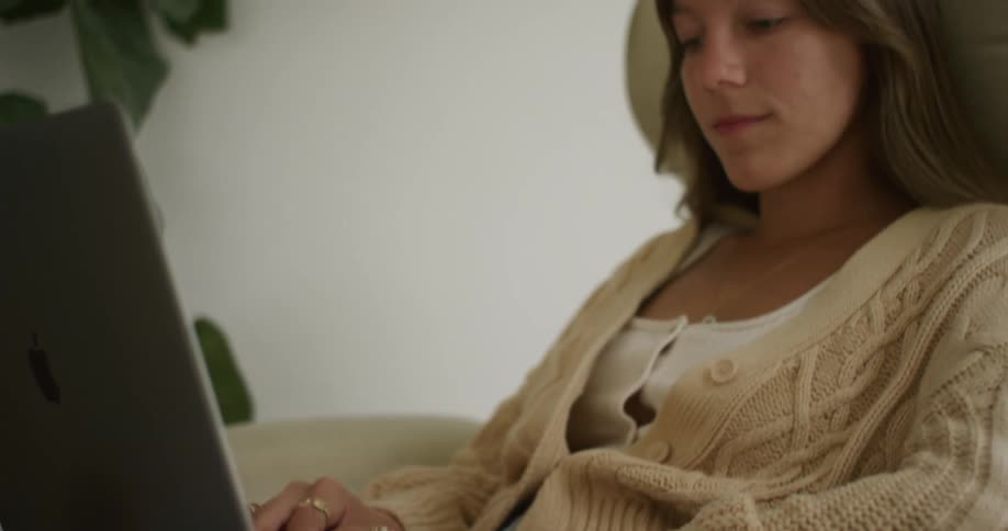 A woman is typing on the laptop in a chair
