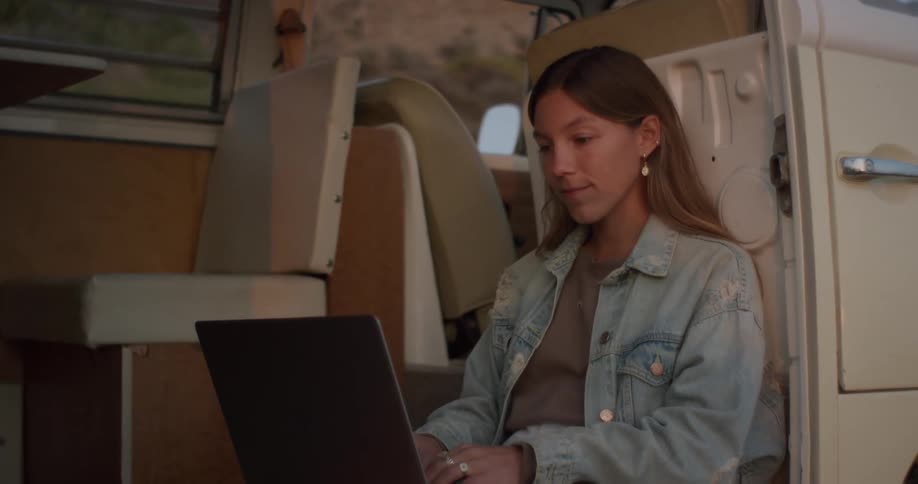 Woman sits in open door of van typing on a laptop