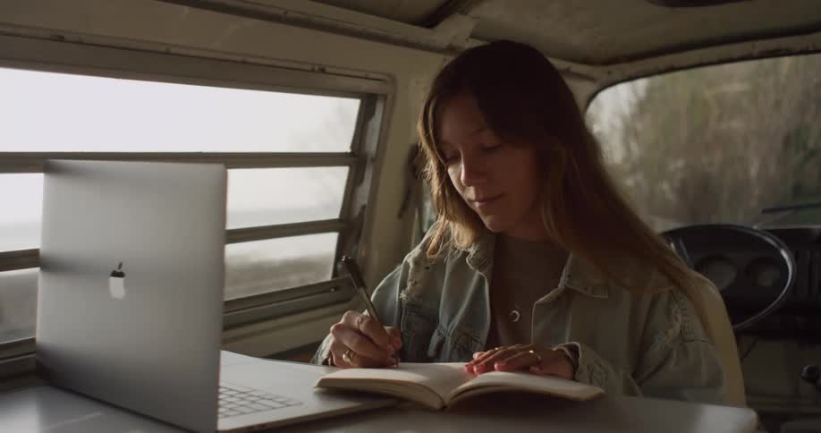 A woman uses her laptop and takes notes in the back of her van