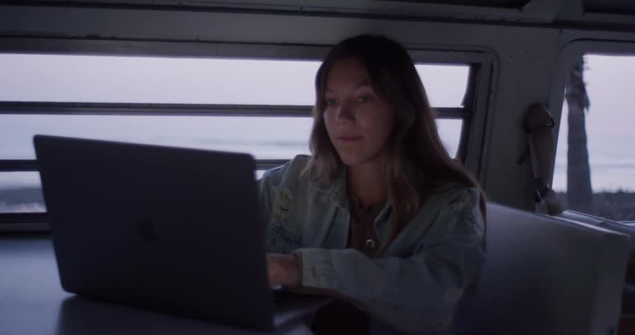 A woman is sitting in the van typing on her laptop