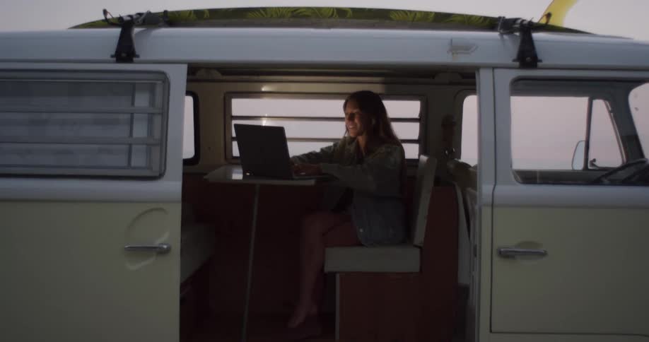 A woman sits in the back of a van and types on a laptop