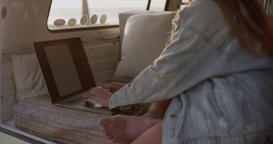 A woman is typing on her laptop in the van