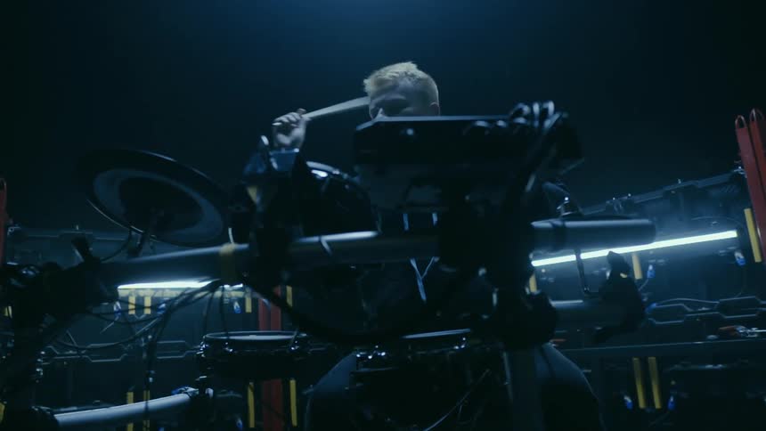 A man playing an electronic drum set under bluish lights