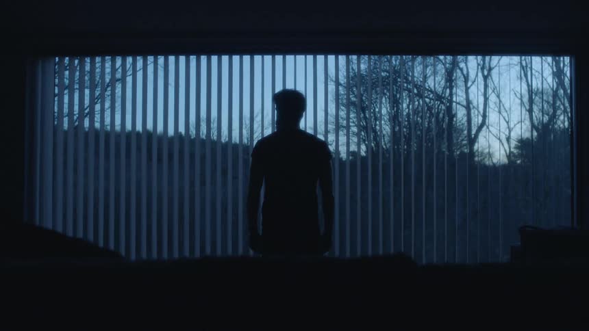 A man looks out the window in the dark room