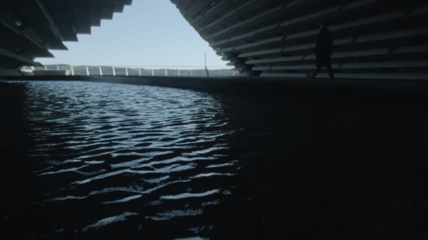 A person is walking near water under a tunnel