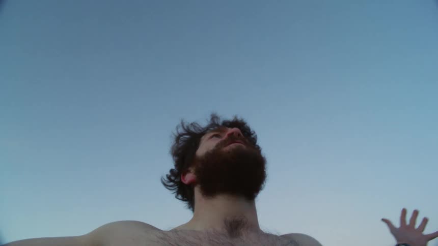 A shirtless man stands outside with his arms outstretched