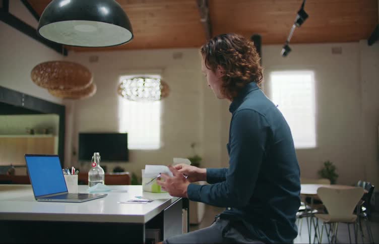 A man sitting at the counter with his laptop on unboxing a covid home test