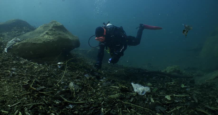 A scuba diver swims close to the floor of the ocean while inspecting an area around a large rock