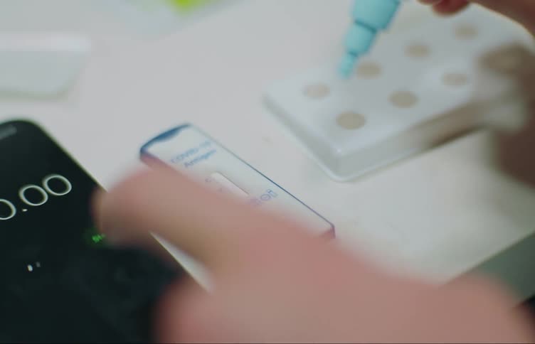A person applies liquid to a medical diagnostic test with a small dropper before setting a timer on their phone