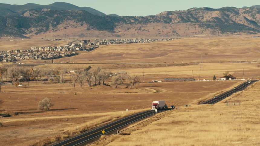 Vehicles trail behind a semi truck driving down a rural highway near mountains