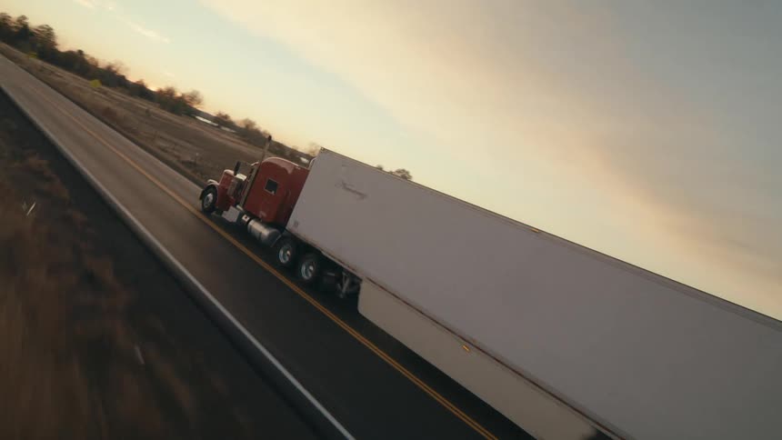 An aerial view following a tractor trailer traveling on a rural twolane highway at dusk