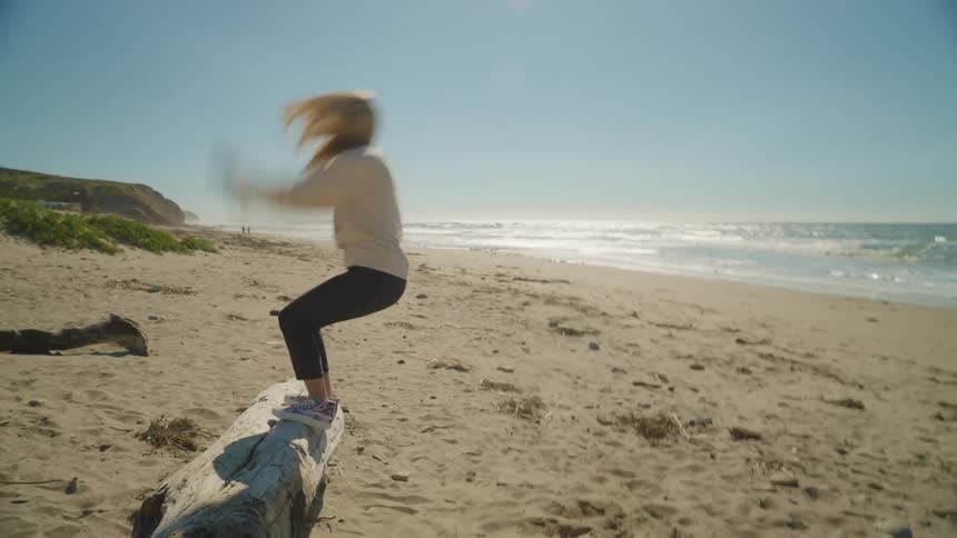 A woman does a backflip off a log on the beach