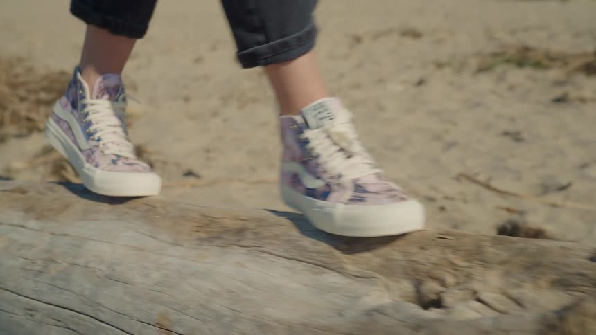 A woman walks on a fallen tree trunk on the beach like a balance beam