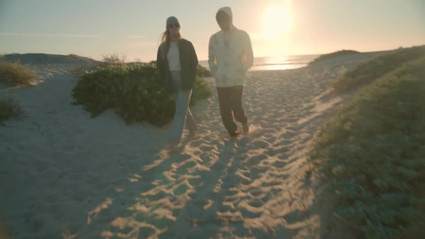 A man and woman on a beach walk away from the water as the sun starts to set
