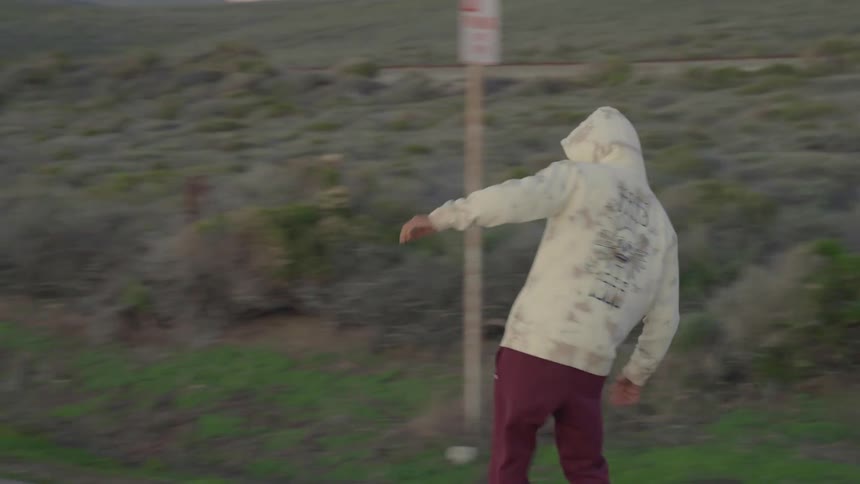 A man skateboards down a coastal road at sunset