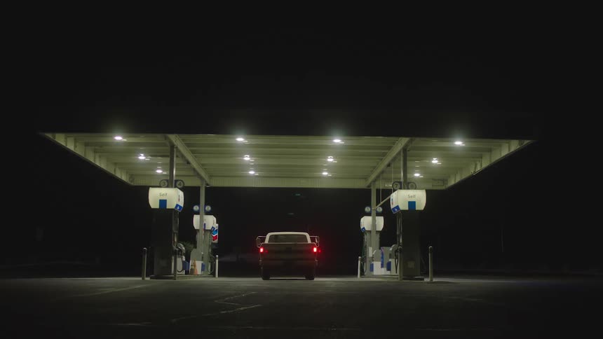 Person drives pickup truck and parks between gas pumps at night