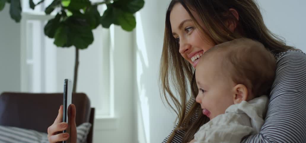 A woman holds her baby and takes a selfie with her smartphone