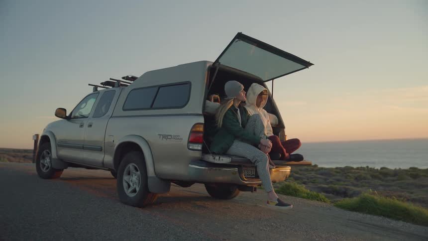 Man and woman are talking while sitting in the back of a truck at dusk