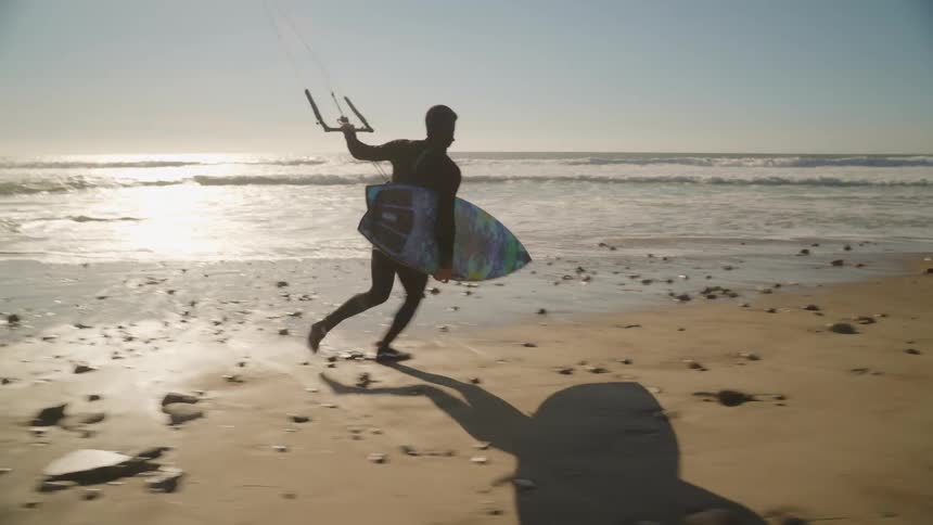 A kitesurfer runs toward the ocean with his board