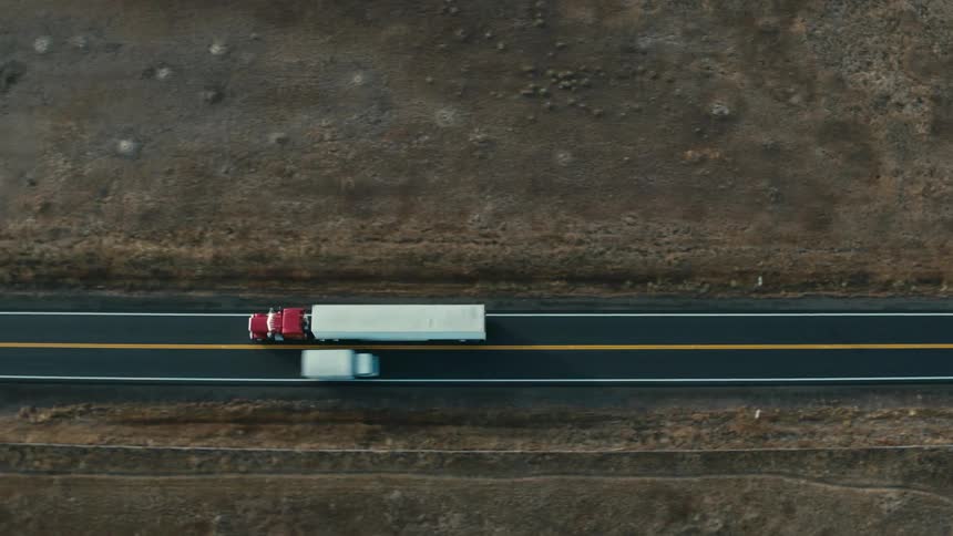 A semi truck passes a box truck on a rural two lane highway