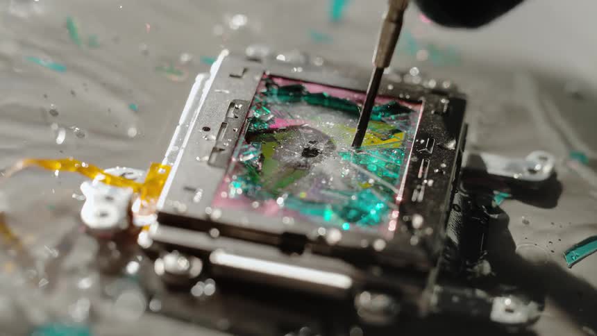 A person uses a small screwdriver to push down on a small screen in water