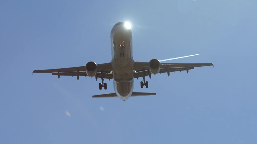 A plane flies high in the sunny sky