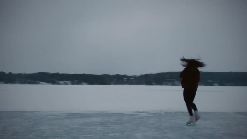 A woman is figure skating on the iced over water