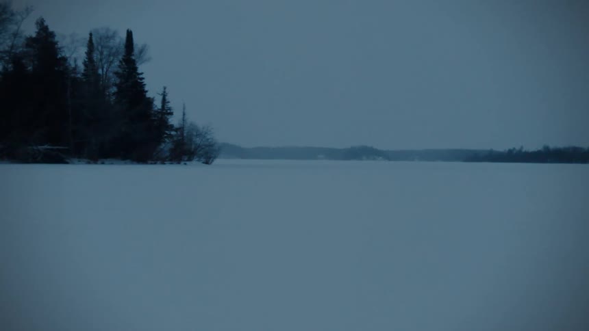 Snow covers a wide open landscape that is dimly lit by the light of the sky above