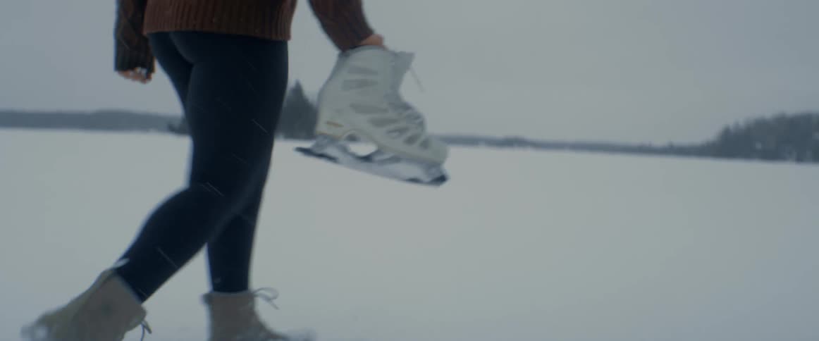 A woman carrying ice skates walks across a snowy field