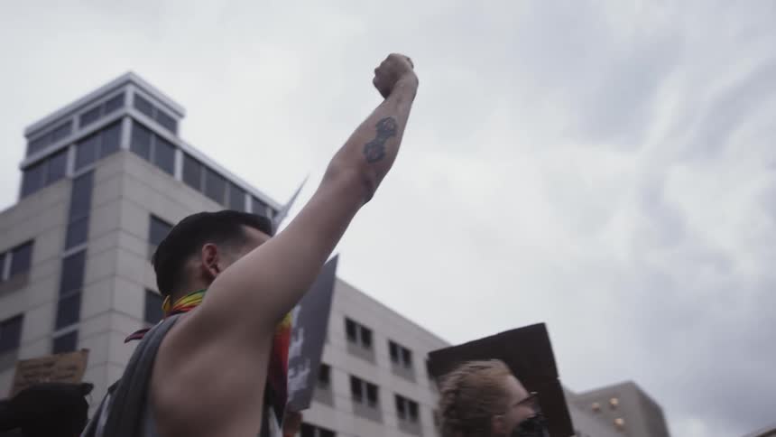 Man with his arm up holds a sign and participates in a protest in a city with others holding signs