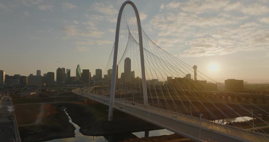 Cars are driving on a bridge near a city while the sun is setting