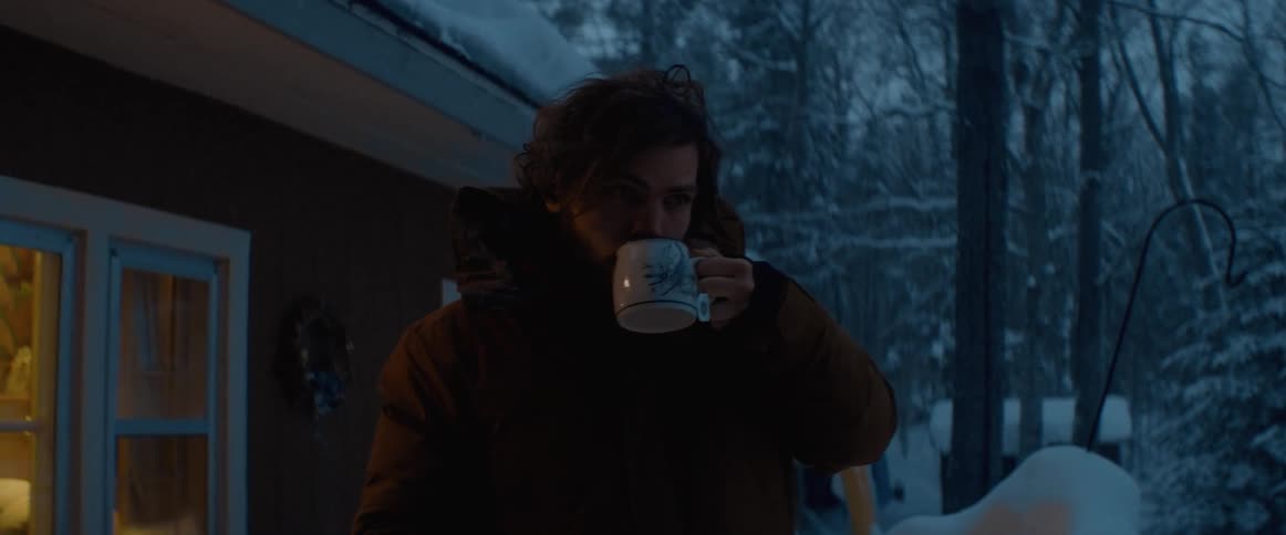A man is drinking coffee outside of his house in winter