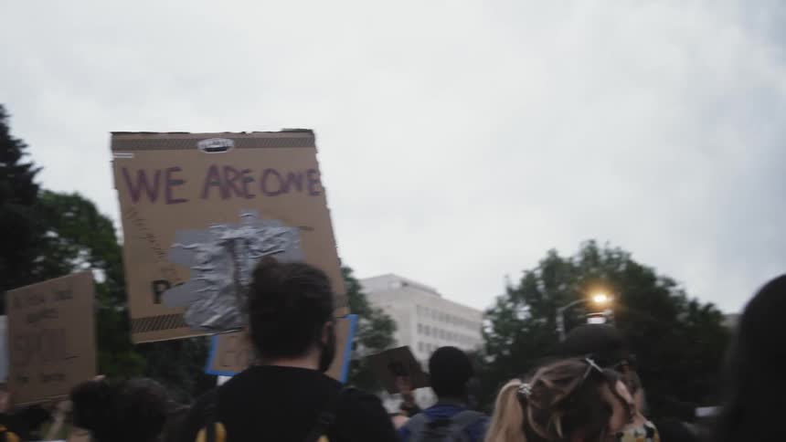 Group of protestors holding up cardboard signs on the city at evening
