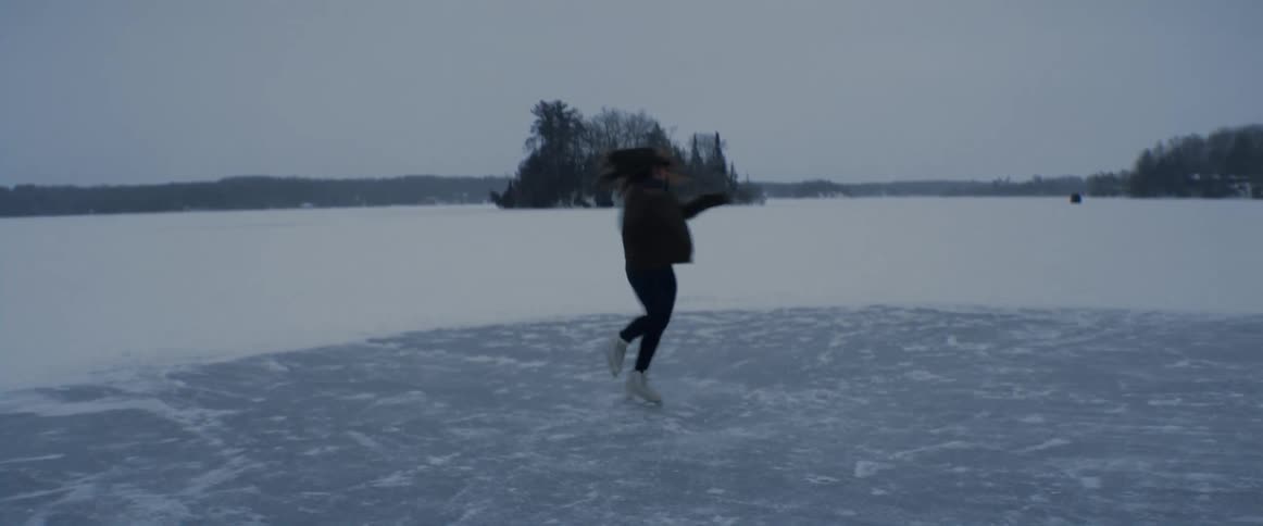 A woman spins and twirls on a frozen lake ice skating on a gray day