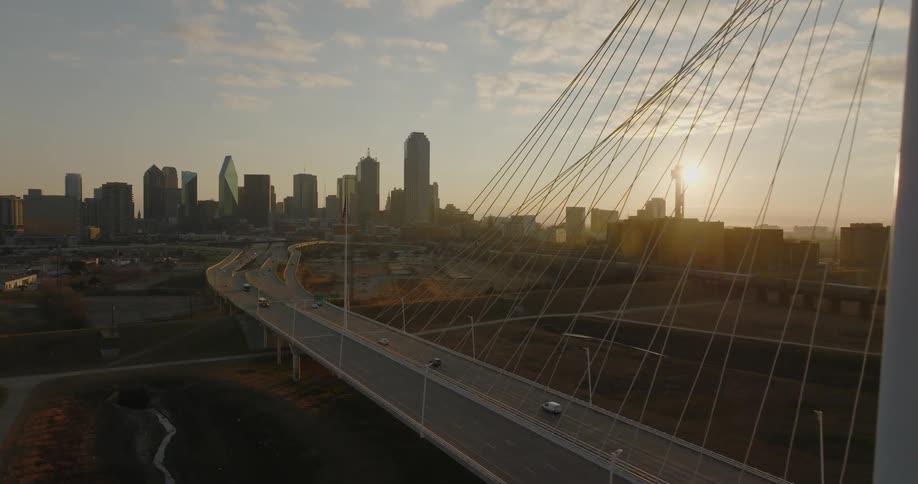 An aerial view of vehicles driving across a bridge with a city skyline in the distance