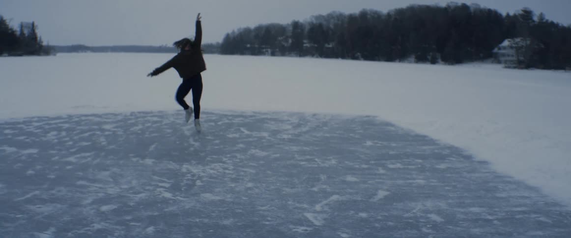 A woman spins and twirls as she ice skates on a frozen lake on a gray day