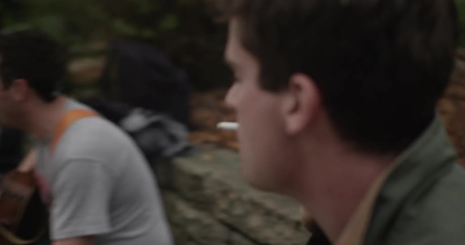 A man smokes and bops his head while another plays a guitar