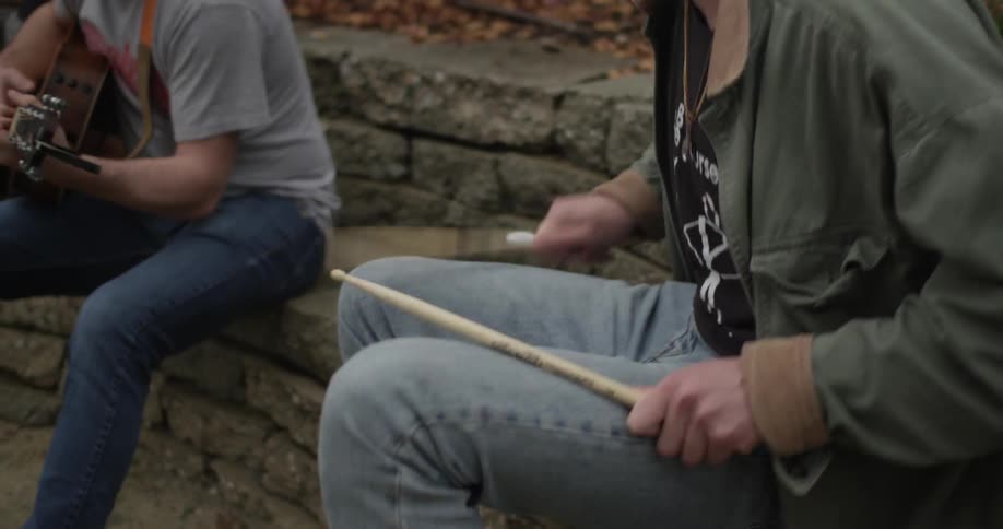 A person drums their legs in time with another person's guitar