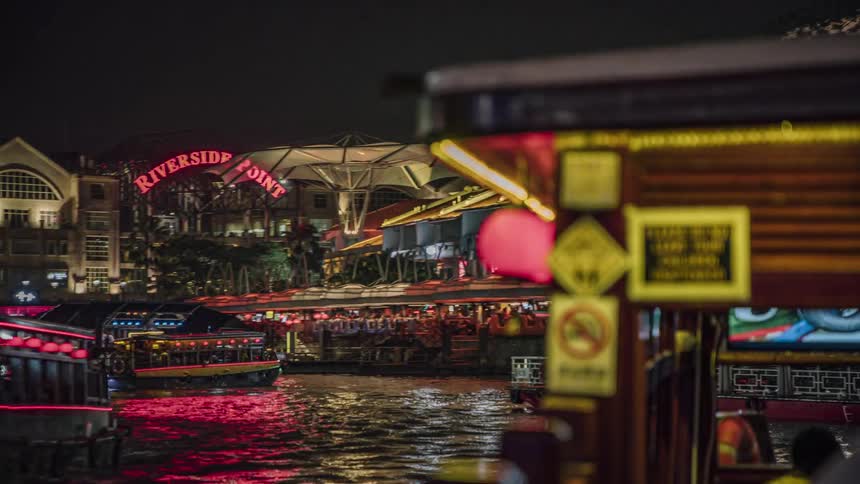Tour boats travel in the river next to the city buildings at night