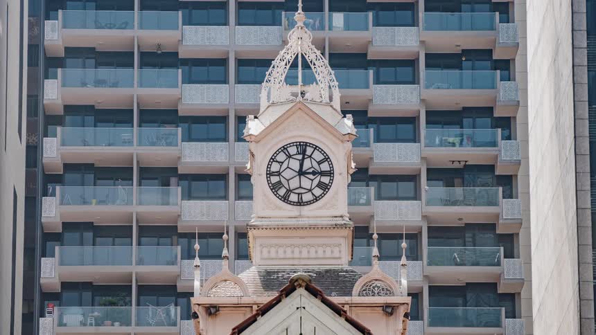 Clock hand rotates around clock in tower standing near apartment building