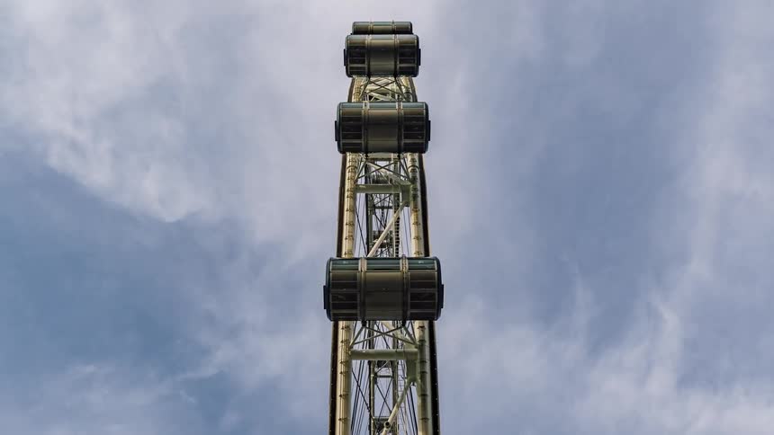 Ferris wheel cars move across cloudy sky as the wheel rotates
