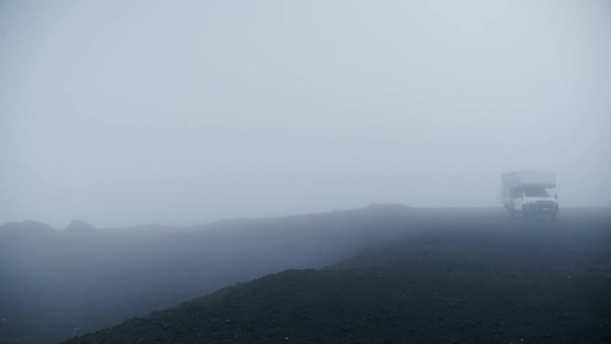 Camper sits parked on dirt near cliff on dense foggy day