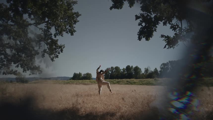Woman wearing white pants and a jacket stands in the field and stretches her arms and legs