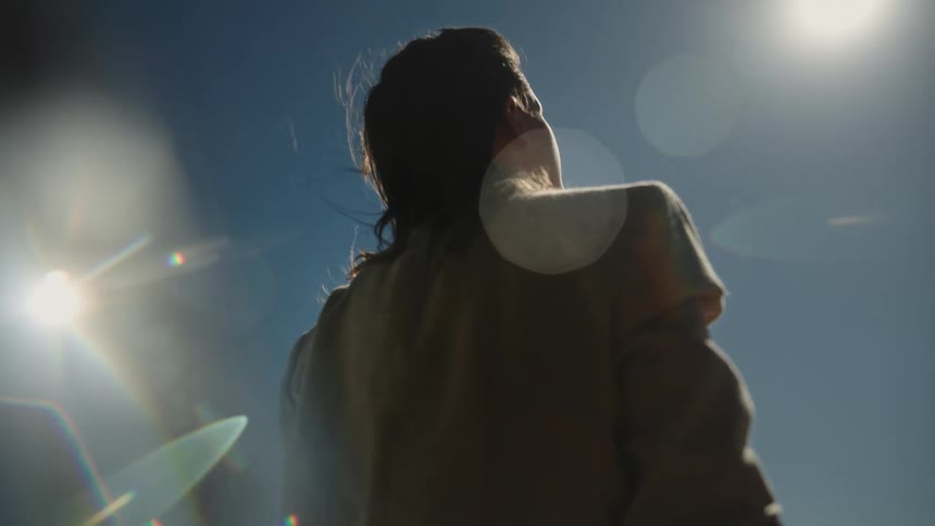 A woman stands outside and looks up at the sky as the sun shines down