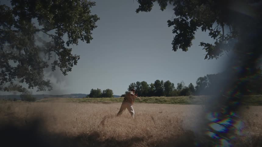 Woman with brown jacket and pants dances in brown grass in the field