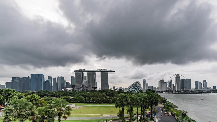 City skyline with skyscrapers ferris wheel and public park next to sea under dark clouds